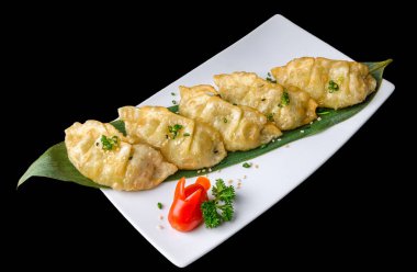 Japon usulü gyoza hamur köfteleri beyaz bir tabakta, yapraklı garnitür ve daldırma sebzeleriyle, siyah arka planda çekiliyor..
