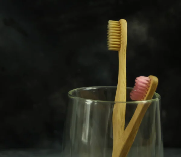 Closeup view of eco-friendly bamboo toothbrushes on a glass on dark background