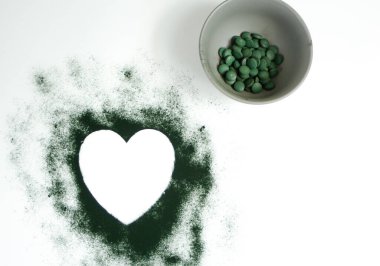 Beyaz arka planda kalp şeklinde spirulina tozu ve tabletler.