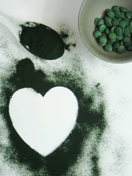 Heart-shaped spirulina powder and tablets on white background