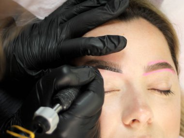 Kozmetik uzmanı, kuaförde çalışan bir müşteriye kaş makyajı yapıyor. Mikroplanma tekniği..