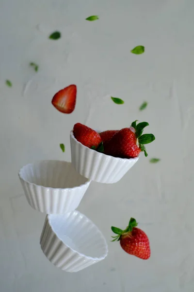 Strawberries in white bowls levitating on the air. Rule of thirds applied
