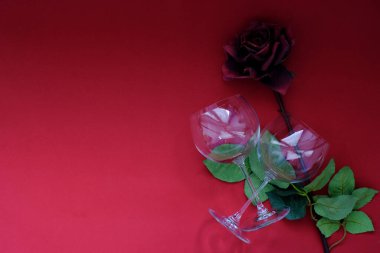Top view of red rose and wine glasses on red background. Minimalist style photography. Flat lay.