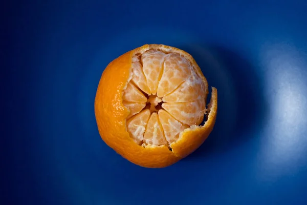 Closeup view of half peeled tangerine on dark blue plate. Minimalist style photography. Color theory. Complementary color theory.