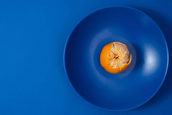 Half peeled tangerine on dark blue plate. Minimalist style photography. Color theory. Complementary color theory.