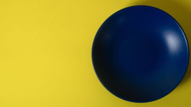 Empty blue plate on yellow background. Flat lay. Copy space. Negative space. Minimalist style photography. Blue and yellow. Complementary color harmony. Color theory