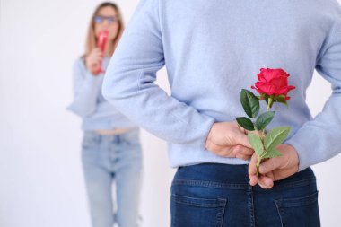 Young attractive man holding a rose behind his back to surprise his lover. Love celebration concept. Date concept. Surprise for her. Happy couple. Elegance. Love. Attraction