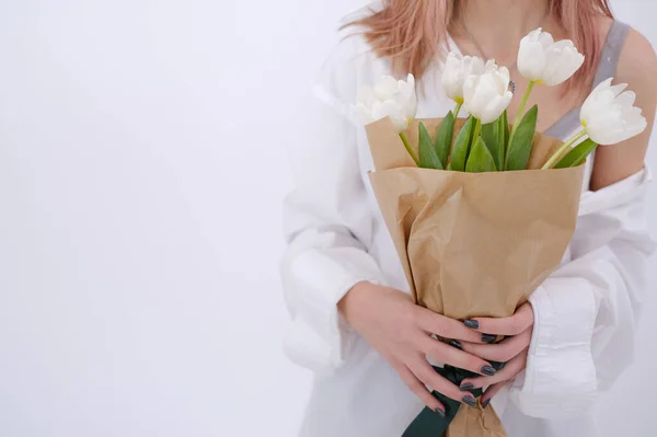 Woman in white shirt holding a bouquet of white tulips in her hands on a white background. Feminine. White shirt. Gift concept for woman, love, birthday, 8 March, mother day. Copy space.