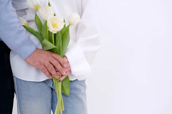 Lovely couple holding each other. Couple hugging. Man hugging woman from the back. A bouquet of tulips on the womans hands. White background. The concept of expressing love. Love celebration. Copy