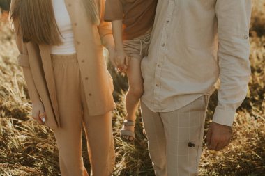 Tarlada yürüyen üç kişilik güzel bir aile. Mutlu büyük aile çayırda gün batımında birlikte oynuyorlar. Aile ve aşk kavramı. Estetik aile gün batımında çocuklarla birlikte yürüyor.