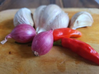 Mutfak tarifleri için baharat ya da aroma malzemeleri. Beyaz sarımsak, acı biber ve ahşap kesme tahtasındaki kırmızı soğan.