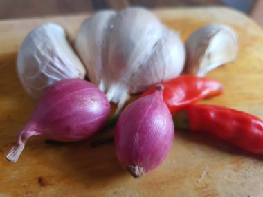 Mutfak tarifleri için baharat ya da aroma malzemeleri. Beyaz sarımsak, acı biber ve ahşap kesme tahtasındaki kırmızı soğan.