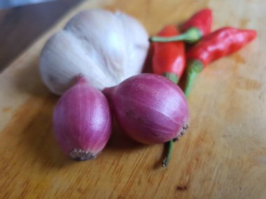 Mutfak tarifleri için baharat ya da aroma malzemeleri. Beyaz sarımsak, acı biber ve ahşap kesme tahtasındaki kırmızı soğan.