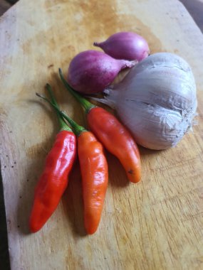 Mutfak tarifleri için baharat ya da aroma malzemeleri. Beyaz sarımsak, acı biber ve ahşap kesme tahtasındaki kırmızı soğan.