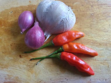 Mutfak tarifleri için baharat ya da aroma malzemeleri. Beyaz sarımsak, acı biber ve ahşap kesme tahtasındaki kırmızı soğan.