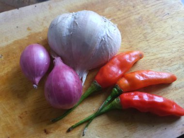 Mutfak tarifleri için baharat ya da aroma malzemeleri. Beyaz sarımsak, acı biber ve ahşap kesme tahtasındaki kırmızı soğan.