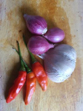 Mutfak tarifleri için baharat ya da aroma malzemeleri. Beyaz sarımsak, acı biber ve ahşap kesme tahtasındaki kırmızı soğan.