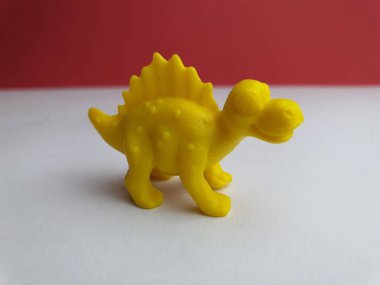 Beyaz zemin üzerinde duran dört bacaklı, jurasik bir yaratığın küçük plastik oyuncağı..