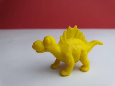 Beyaz zemin üzerinde duran dört bacaklı, jurasik bir yaratığın küçük plastik oyuncağı..