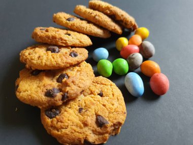 Siyah arkaplanda renkli şeker topları ve kurabiye süsü.