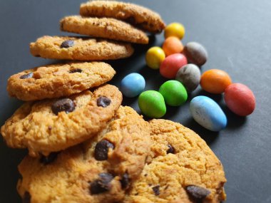 Siyah arkaplanda renkli şeker topları ve kurabiye süsü.