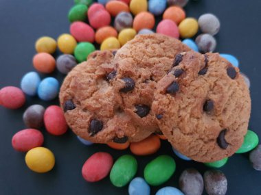 Siyah arkaplanda renkli şeker topları ve kurabiye süsü.