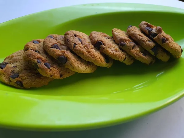 チョコレートチップクッキー 白い表面の背景に置かれた緑の葉の形をした皿板 — ストック写真
