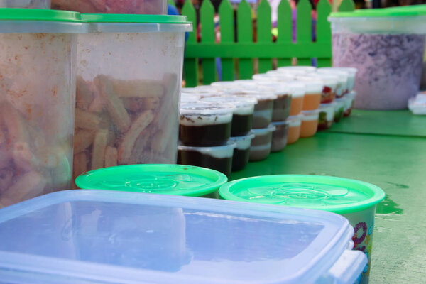 Puddings in plastic containers are placed on a green table, sold by street vendors