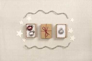 Yukarıdan üç küçük kahverengi kağıt hediye kutusunda noel süsleri ve kırmızı papyon, dekoratif yıldızlar ve çizgili kağıtta dalgalar.