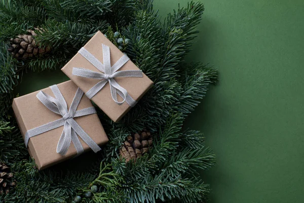 两个有领结的褐色纸盒 放置在圣诞花圈中央 用长矛枝和松果制成 绿色背景 并有彩色背景 — 图库照片