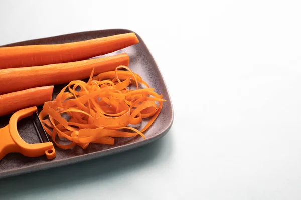 Nahaufnahme Von Drei Geschälten Karotten Und Karottenschalen Auf Grauem Teller — Stockfoto