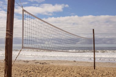 Kaliforniya 'nın kumlu sahilindeki tahta direklere bağlı plaj voleybolu ağı. Dalgalar, okyanus ve arka planda beyaz bulutlar olan gökyüzü.