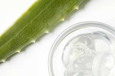Top view closeup of clear glass bowl with aloe vera gel on white background with green aloe leaf