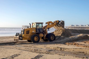 Excavator pushing sand into a pile to preserve the sand from being washed away into the ocean. Near Crystal Pier, Pacific Beach, San Diego on January 6, 2023