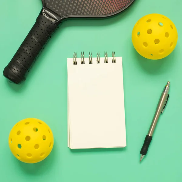上からライトグリーンの背景にピックボール ラケット ペンと白の空白のメモ帳で表示されます 正方形のフォーマット コピースペース付き — ストック写真