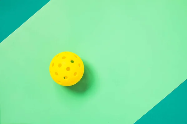 Top view on a bright yellow pickleball on light green and turquoise background with copy space