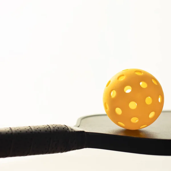 Bright yellow pickleball on top of the raquet with white background and copy space. Square format.