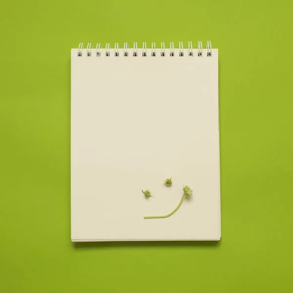 Top view on blank white notepad with a smily face made of tiny flowers, with bright chartreuse green background. Square format.