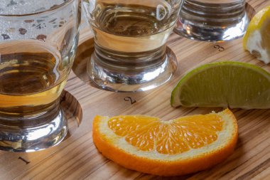 Tekilayla doldurulmuş üç bardağın yakın görüntüsü, tahtanın üzerinde numaralar ve meyve dilimleri var.