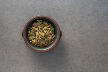 Yeşil pepitaların üst görüntüsü balkabağı tohumlarını beton yüzeyde yeşil ve turuncu bir kâsede fotokopi alanı ile kapatır.