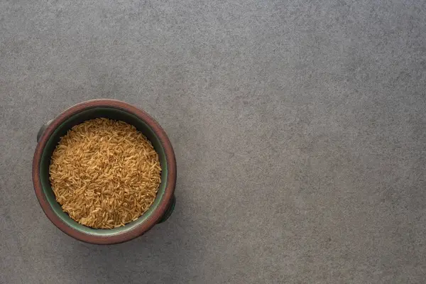 Beton yüzeyde kahverengi pirinç taneleriyle dolu kil yeşil bir kasenin üst görüntüsü.