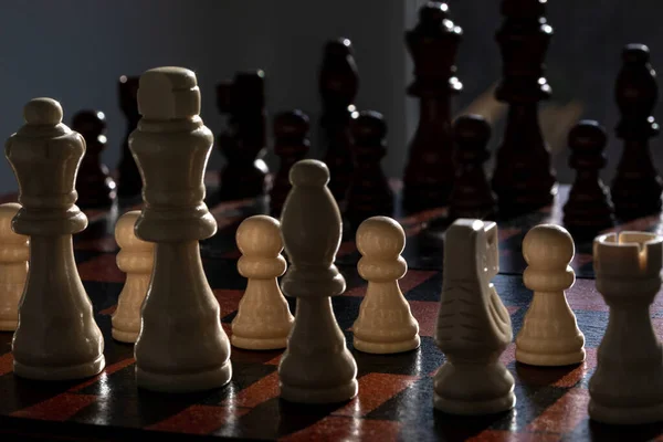 Satranç tahtasındaki beyaz satranç figürlerinin yakın görüntüsü, arka planda siyah figürler bulanıklaşıyor.