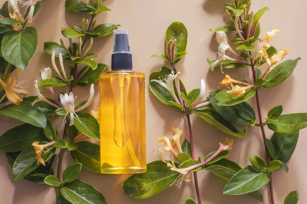 stock image Flatlay closeup of a clear glass bottle with a skin care oil and vines with flowers on light pink background. Bodycare mockup