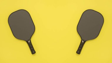 Yukarıdan, parlak sarı arka planda iki picleball raketinden bak. Fotokopi alanı olan afiş veya poster