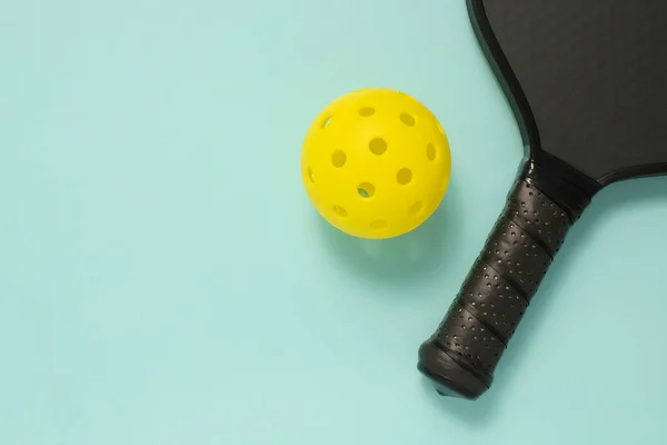 Pickleball raketi ve açık mavi arka planda fotokopi alanı olan sarı topun yukarıdan yakın görüntüsü. Spor afişi ya da afiş