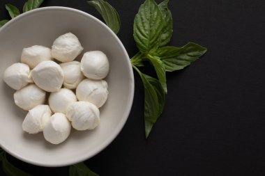 Siyah zemin üzerinde taze mozzarella ve fesleğen yaprakları olan bir kasenin üst görüntüsü.