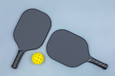 Closeup top view of two black pickleball paddles and a yellow ball on light gray background with copy space clipart