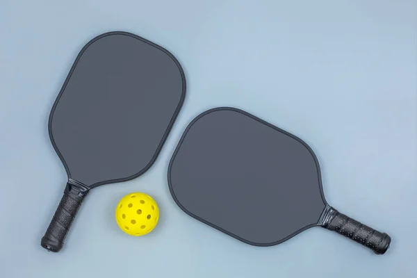 2つの黒いピックルボールパドルとコピースペースとライトグレーの背景に黄色のボールの上ビューを閉じます — ストック写真