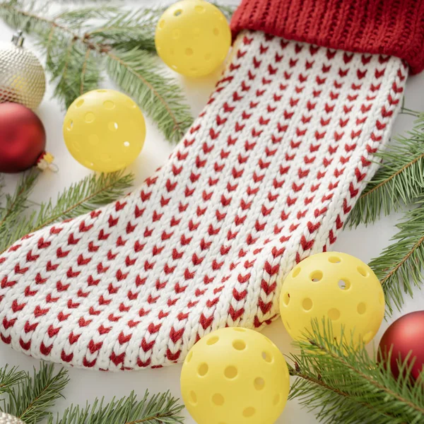 Beyaz ve kırmızı örülmüş Noel çorabının beyaz arka plandaki çam dalları, süslemeleri ve pena toplarıyla yakın görüntüsü. Kare bileşimi