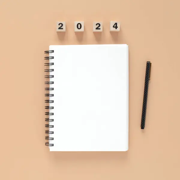 Close top view of a white blank page of a spiral notebook and a pen for 2024 year on peach orange color background. Trendy color of the year. Square composition.